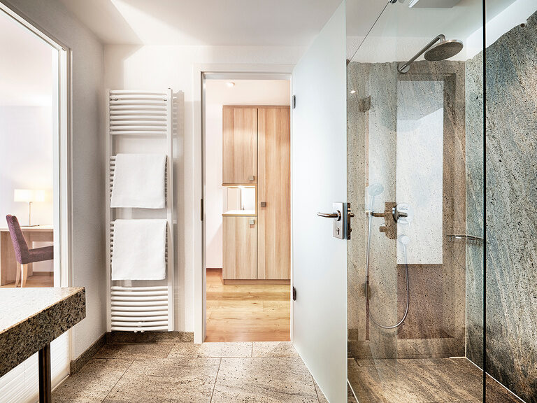 Die Badezimmer dieser Kategorie verfügen über eine große Partnerdusche aus Granit sowie über eine separate Toilette Das schicke und edle Bad der Traumbett-Juniorsuite im Hotel Kronelamm.