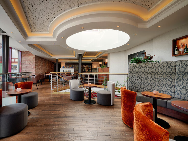 Lichtdurchflutete, modern eingerichtete Räumlichkeit mit Sesseln, Tischen und Bücherregal.