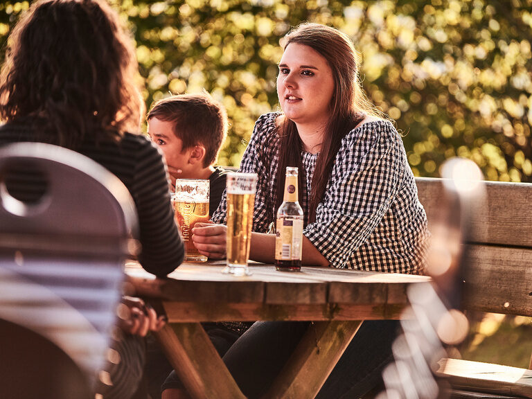 Drei Gäste sitzen an einem Biertisch und trinken erfrischende Getränke.