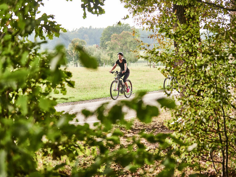 A young woman wearing a bicycle helmet rides a mountain bike on a well-developed path
