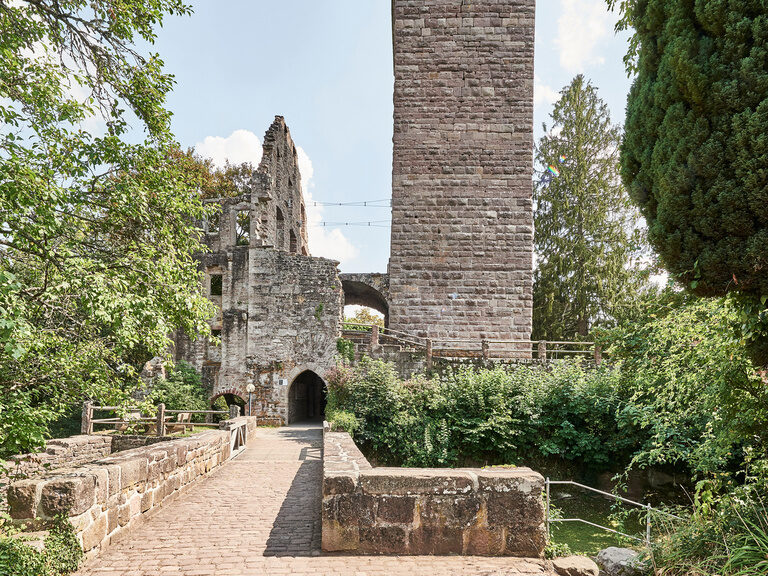 In der Umgebung des Hotels in Zavelstein finden sich viele Möglichkeiten für ein abwechslungsreiches Rahmenprogramm für Tagungen. Ein gepflasterter Weg führt über eine Brücke zu einer Burgruine, die von Bäumen umrahmt ist.