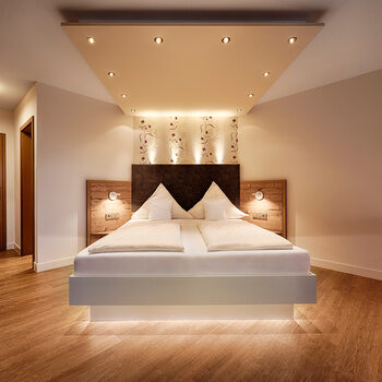 Ein weißes, beleuchtetes Bett und ein roter Sessel in einem Hotelzimmer mit Holzboden und Holztüren.