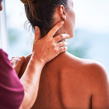 Eine Dame wird von einer Masseurin im Nackenbereich massiert.