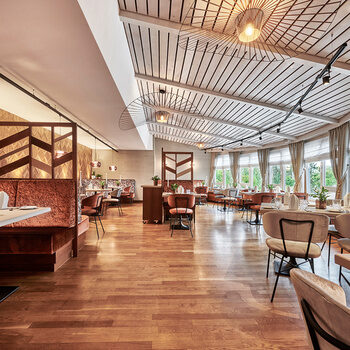 Ein modernes und helles Restaurant im Hotel Kronelamm mit großen Fenstern, die eine herrliche Aussicht bieten. Geschmackvoll eingerichtete Sitzbereiche mit stilvollen Trennwänden und warmen Holzelementen schaffen eine einladende Atmosphäre.