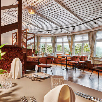 Stilvoll gedeckter Tisch im Restaurant des Hotel Kronelamm Ein elegant gedeckter Tisch im Restaurant des Hotel Kronelamm, mit Blick auf die großen Fenster und die gemütlichen Sitzbereiche. Die Einrichtung ist modern mit warmen Farbtönen, Pflanzen und viel Tageslicht.