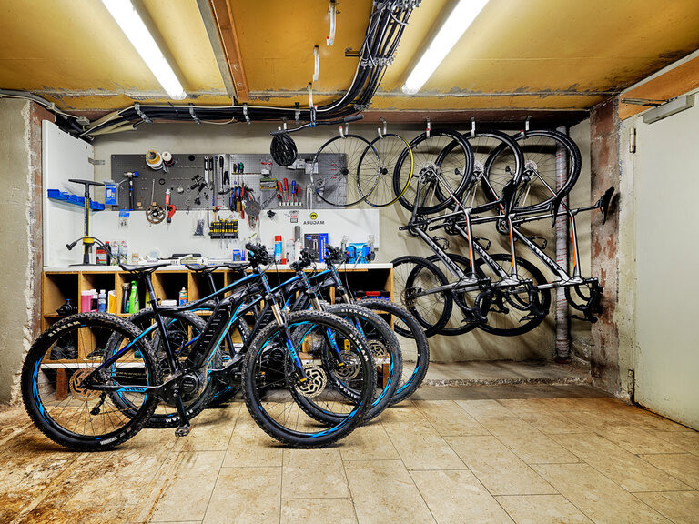 In einem Raum stehen und hängen Mountainbikes verschiedener Größen sowie Elektrobikes.