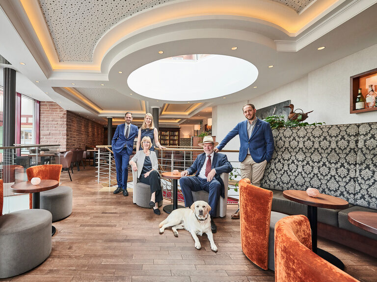 The Berlin family with their dog Prinz, standing and sitting on the modern, orange and gray armchairs, in the lounge.