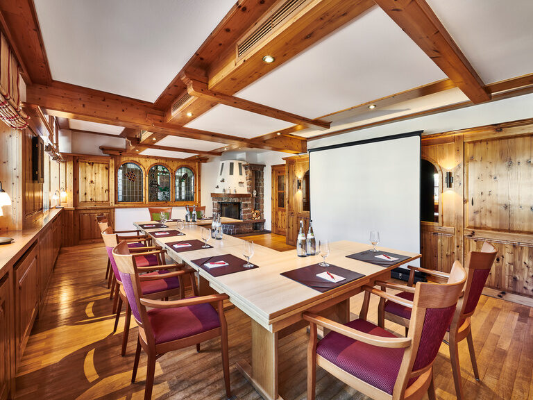 In a historic room with a fireplace there are tables and chairs as well as a screen and projector.