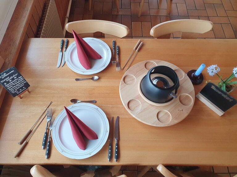 Ein Fondueabend im Zavelsteiner Wanderheim verspricht urgemütliche Stunden. Ein eingedeckter Tisch mit Tellern, Besteck und Fonduetopf.