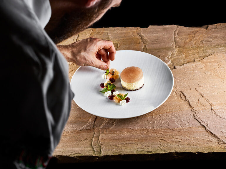 A chef garnishes a dessert on a white plate on a stone slab.