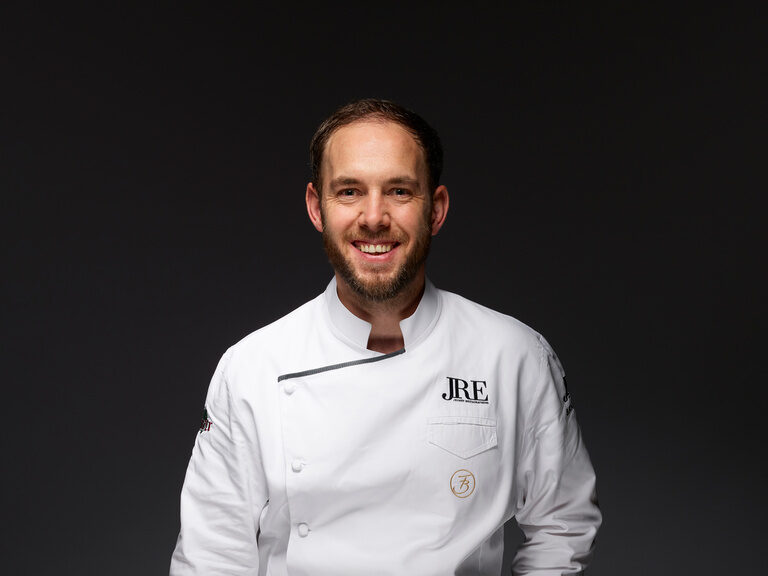 Sternekoch Franz Berlin kehrte, zur Neuausrichtung des gut bürgerlichen Restaurants Krone, 2009 zurück in den elterlichen Betrieb. Franz Berlin, in weißer Kochjacke, lächelnd vor einem dunklen Hintergrund.