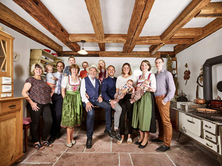 Familie Berlin des Wellnesshotels Kronelamm im Schwarzwald lädt Sie ein zum Königin und König sein in Zavelstein. Gastgeberfamilie Berlin sowie alle weiteren Familienmitglieder stehen in einem Raum, der einer alten Küche gleicht.