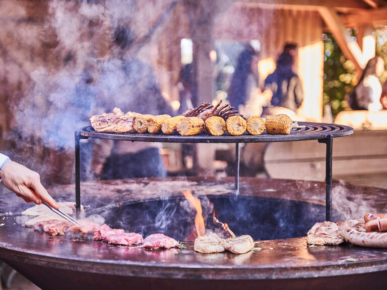 Mehrere verschiedene Speisen liegen auf einem Grill mit Grillmeister im Hintergrund