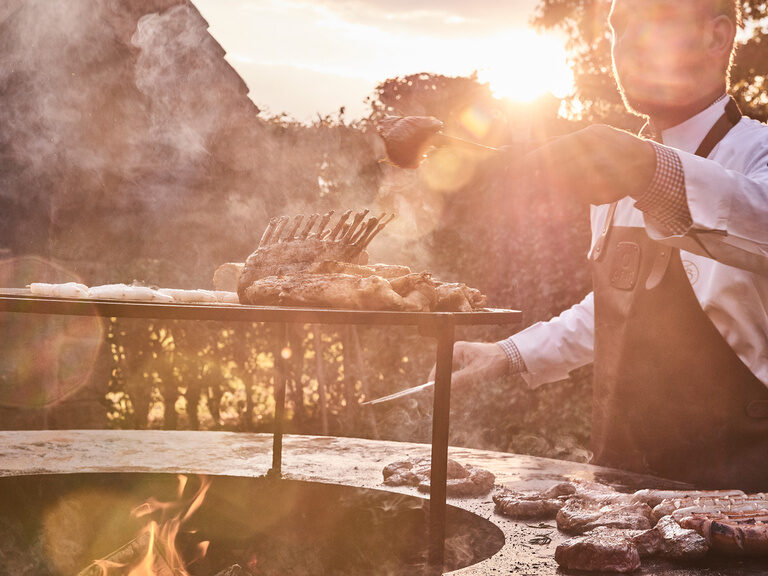 A grill master takes care of various dishes on a grill