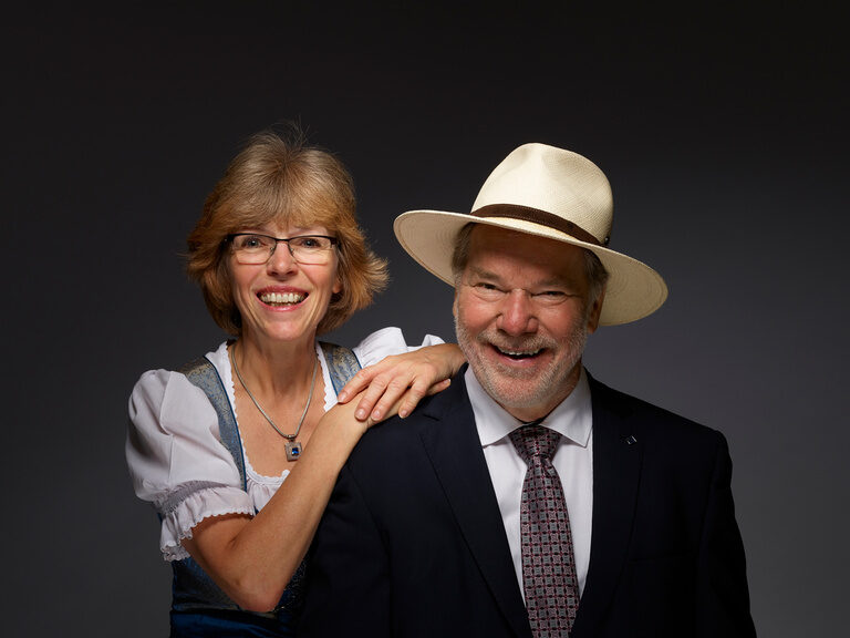 Seniorchefin Gudrun und Seniorchef Rolf Berlin gründeten 1994 das Hotel Kronelamm im Schwarzwald, welches seither kontinuierlich erweitert und erneuert wurde. Seniorchefin Gudrun und Seniorchef Rolf Berlin lächelnd vor einem schwarzen Hintergrund.