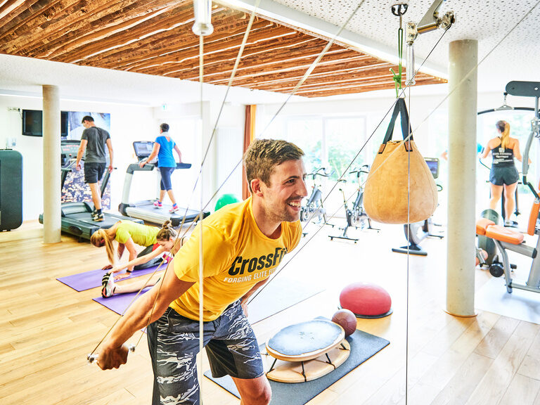 A young man and other guests are training on various sports equipment in a fitness room.
