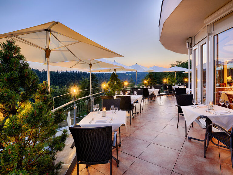 Gemütliche Abendstimmung auf der Panoramaterrasse des Hotelrestaurants Kronelamm im Schwarzwald. Eingedeckte Tische mit Stühlen aus der Terrasse mit Sonnenuntergang.