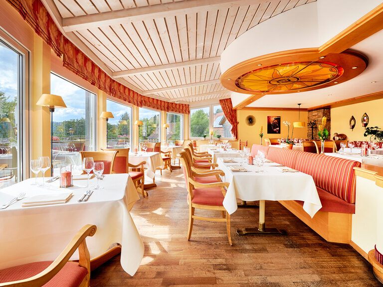 Lichtdurchflutete Stube mit eingedeckten Tischen, Stühlen und Bänken, die in rot gehalten sind.