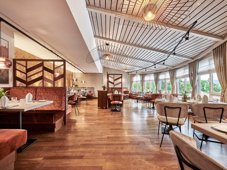Helles und elegantes Hotelrestaurant im Hotel Kronelamm Ein modernes und helles Restaurant im Hotel Kronelamm mit großen Fenstern, die eine herrliche Aussicht bieten. Geschmackvoll eingerichtete Sitzbereiche mit stilvollen Trennwänden und warmen Holzelementen schaffen eine einladende Atmosphäre.