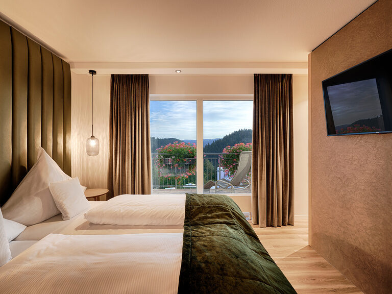Ein komfortables Bett steht vor einem großen Panoramafenster, das die Idylle des Schwarzwalds zeigt.