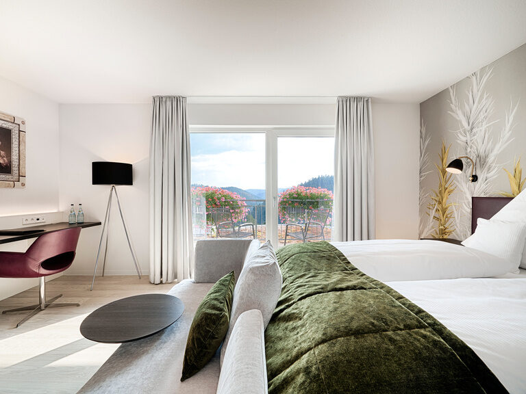Die Komfort-Doppelzimmer Talblick liegen sehr ruhig zur Südseite des Hotels Kronelamm in Zavelstein. Ein großzügiges Bett, auf dem weiße Bettwäsche und eine grüne Tagesdecke liegt in einem lichtdurchfluteten Hotelzimmer.