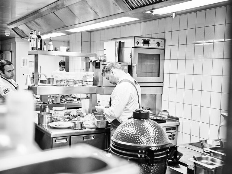 In einer Restaurantküche arbeiten drei Köche zwischen diversen Kochutensilien und Lebensmitteln.