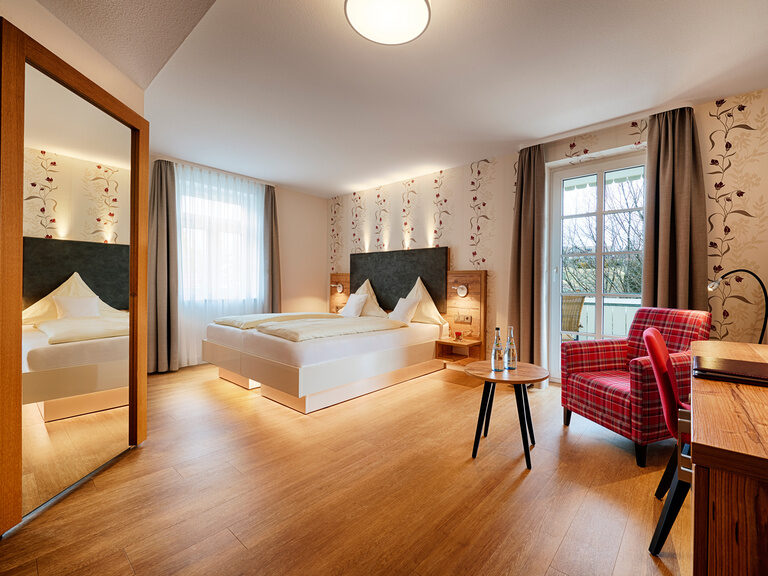 A comfortably furnished hotel room with a large bed, armchair and desk.