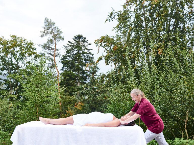 Bestens ausgebildete Mitarbeiter:innen kümmern sich im Wellnesshotel Kronelamm im Schwarzwald um entspannende Massagen und kosmetische Anwendungen. Frau auf einer Massageliege im Außenbereich des königSpa bekommt eine Massage