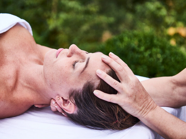 Lying down, a young woman's head is being massaged by one hand.