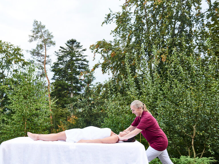 Eine Frau liegt auf einer Massageliege im Aussenbereich des königSPA und bekommt eine Massage.