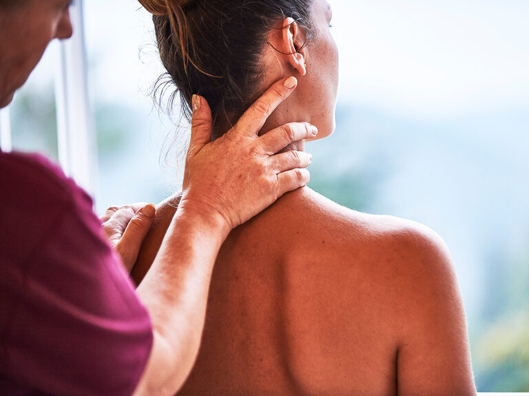 Eine Dame wird von einer Masseurin im Nackenbereich massiert.