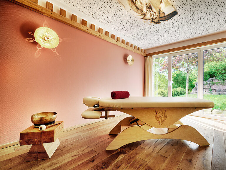 Eine hölzerne Massageliege mit bequemer Auflage steht in einem harmonischen Raum im königSpa des Wellnesshotels Kronelamm Im Schwarzwald.