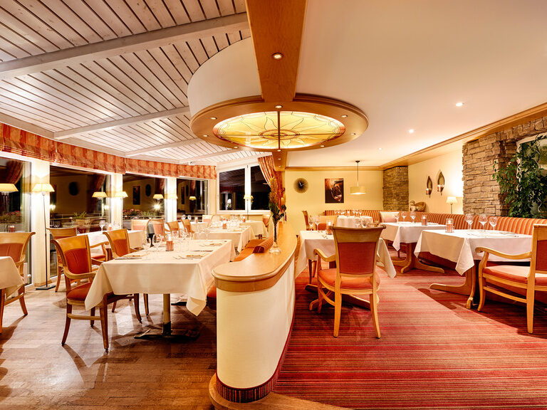 A room decorated in red tones with set tables, chairs and upholstered benches at night.