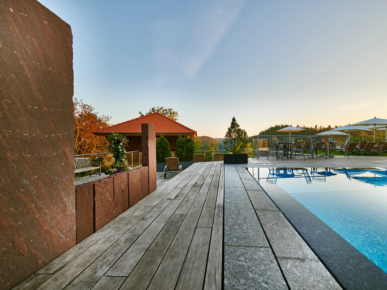Outdoor area of the wellness area with outdoor pool, high-seat sauna, sunbathing area and panoramic views of the Black Forest.
