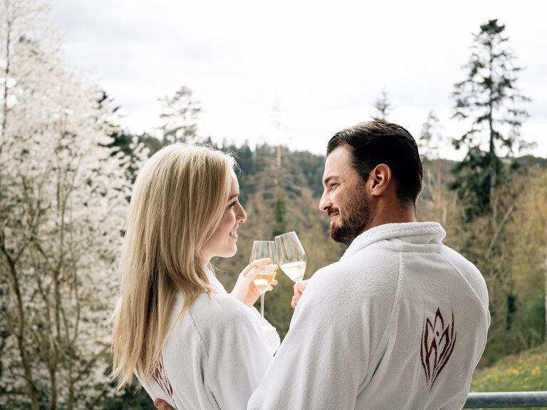 Ein junges Hotelgästepaar im Bademantel stößt mit einem Glas sekt an.