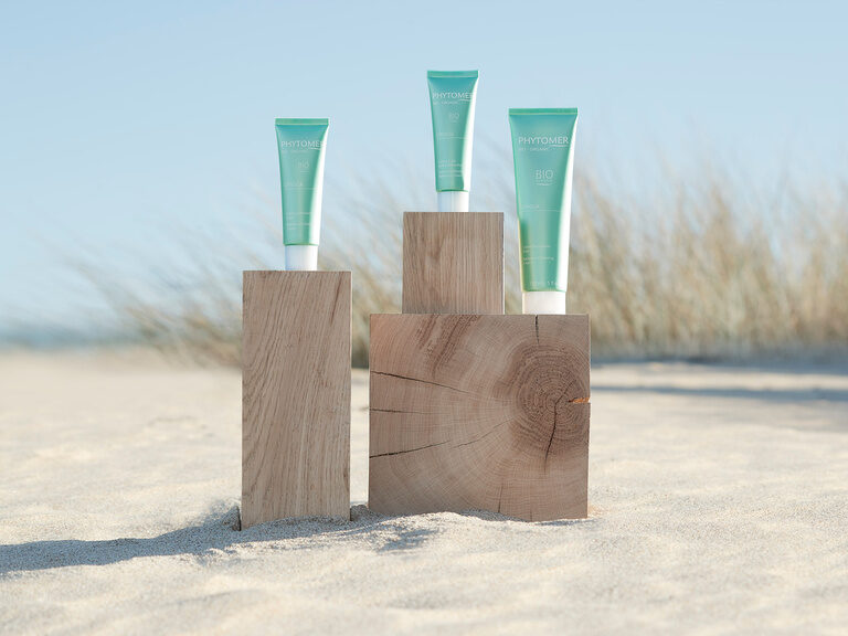Das Unternehmen PHYTOMER steht für gesunde, respektvolle und nachhaltige Schönheit. Drei Produkte der Marke Phytomer sind auf einem Strand trappiert.