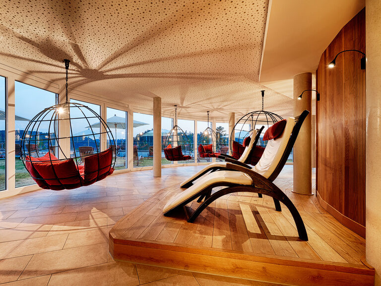 A large relaxation room with panoramic windows with a view of the Black Forest, as well as hanging chairs and wellness loungers.