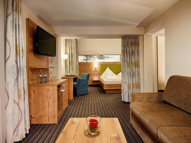 Hotel room furnished in a country house style with amenities such as a double bed, couch, desk, armchair and television.