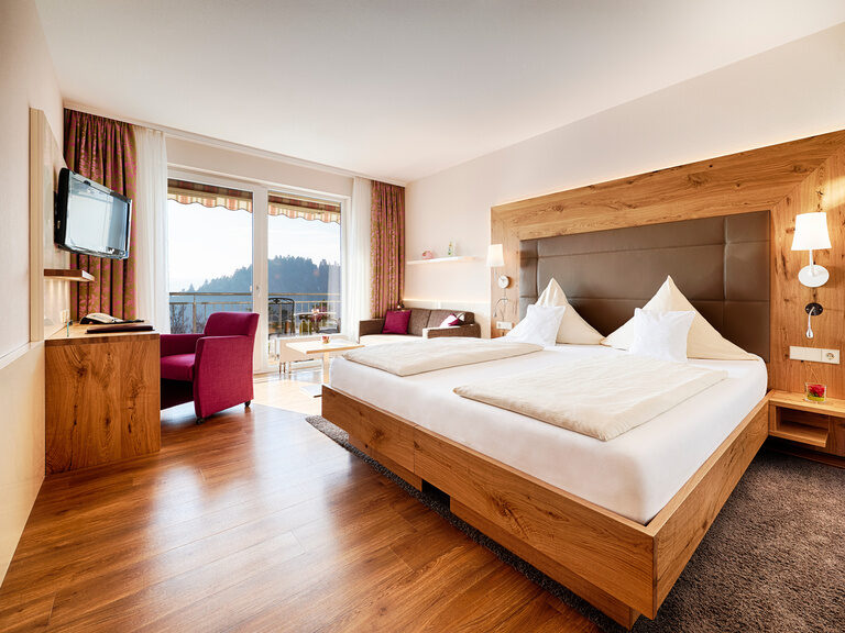 Room with double bed, desk, armchair and large panoramic windows.