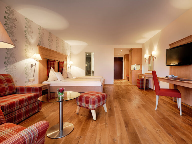 Modernly furnished, very large hotel room with double bed, desk, cosmetic table and comfortable seating.