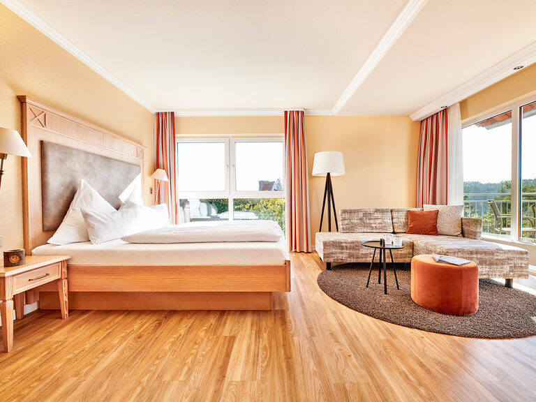 Die Zimmer liegen auf der Südseite im Hotel Kronelamm in den oberen Stockwerken mit Balkon und grandioser Aussicht über den Pool und den Schwarzwald. Der helle Schlafbereich mit Mobiliar im Deluxe Zimmer Talblick am Tag.