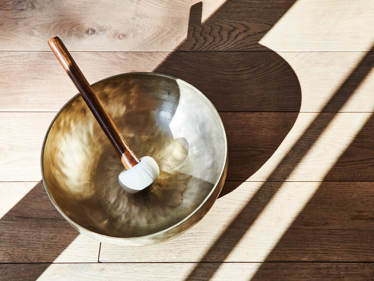 A singing bowl with a mallet stands on a wooden floor