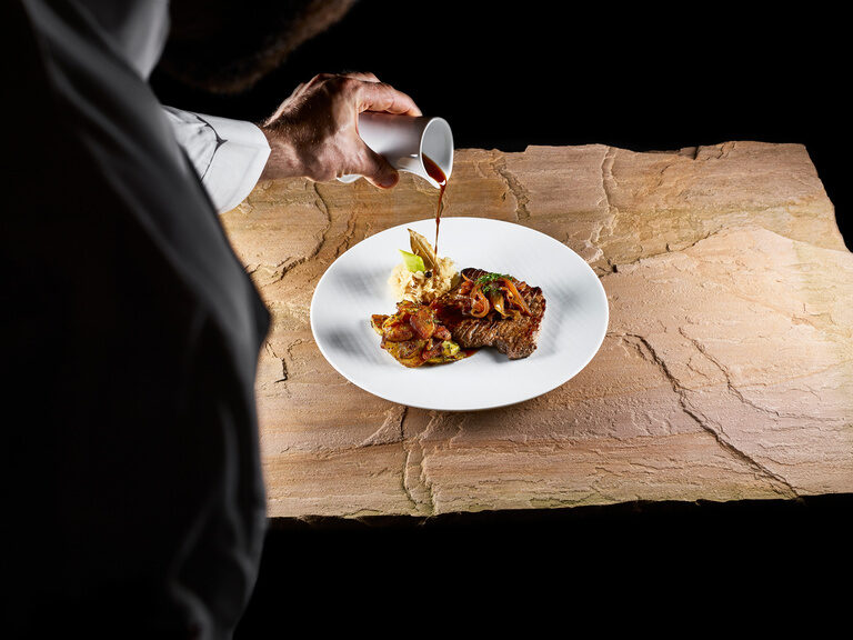 Regionalität, Qualität, Herkunft und schonender Umgang mit Lebensmitteln sind in den Küchen des Hotels eine Selbstverständlichkeit Ein Zwiebelrostbraten auf einem Weißen Teller angerichtet, welcher auf einer Steinplatte steht.