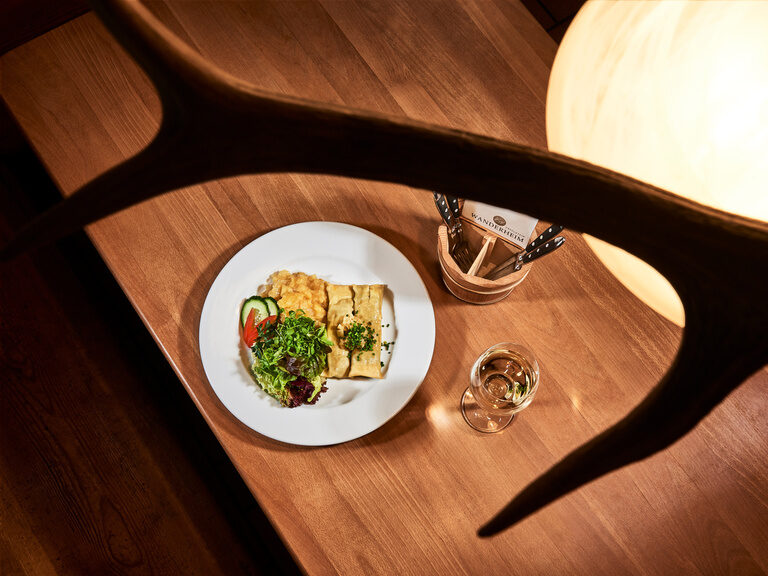 Hausgemachte Maultaschen nach traditionellem Rezept von Rolf Berlin mit Zwiebelschmelze, Kartoffelsalat und Rohkost- und Blattsalate. Ein Teller mit Maultaschen, Kartoffelsalat auf einem weißen Teller angerichtet. Neben dem Teller steht ein Glas Weißwein.