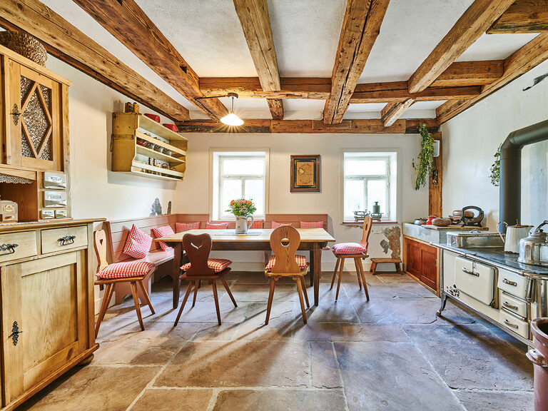 Die originalgetreue Stube "Küche" lädt zum gemütlichen Beisammensein ein und erinnert an die frühere Zeit. Eine Stube mit einem Tisch, verschiedenen Stühlen, rustikalen Schränken, einer alten Küchenzeile und gemütlichen Details.