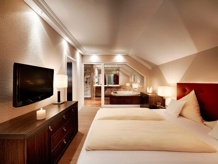 Die exquisit und modern eingerichtete Suite im Haupthaus Hotel Kronelamm eignet sich bestens für besondere Momente zu zweit. Ein großzügiges Zimmer mit gemütlichem Doppelbett, das an das Badezimmer mit Whirlpool angrenzt.