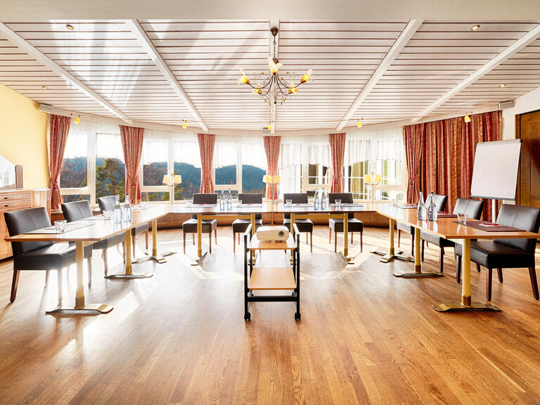 In einem lichtdurchfluteten Raum, mit Blick in den Schwarzwald, stehen Tische und Stühle in U-Form.