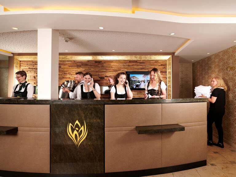 Die Hotelrezeption des Hotels Kronelamm im Schwarzwald steht allen Gästen bei Fragen, Wünschen und Anregungen jederzeit zur Verfügung. Vier Empfangsmitarbeiterinnen, die telefonieren und arbeiten stehen an der Rezeption.