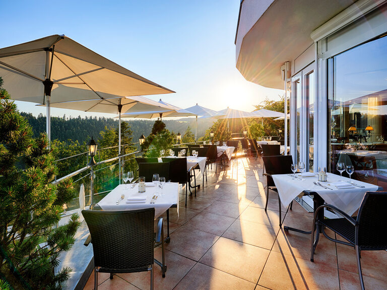 Tables and chairs set in bright sunshine on the restaurant terrace.