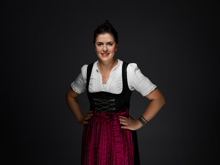 Veranstaltungsleiterin, Tugba Aslan, im Dirndl bekleidet vor einem dunklen Hintergrund.